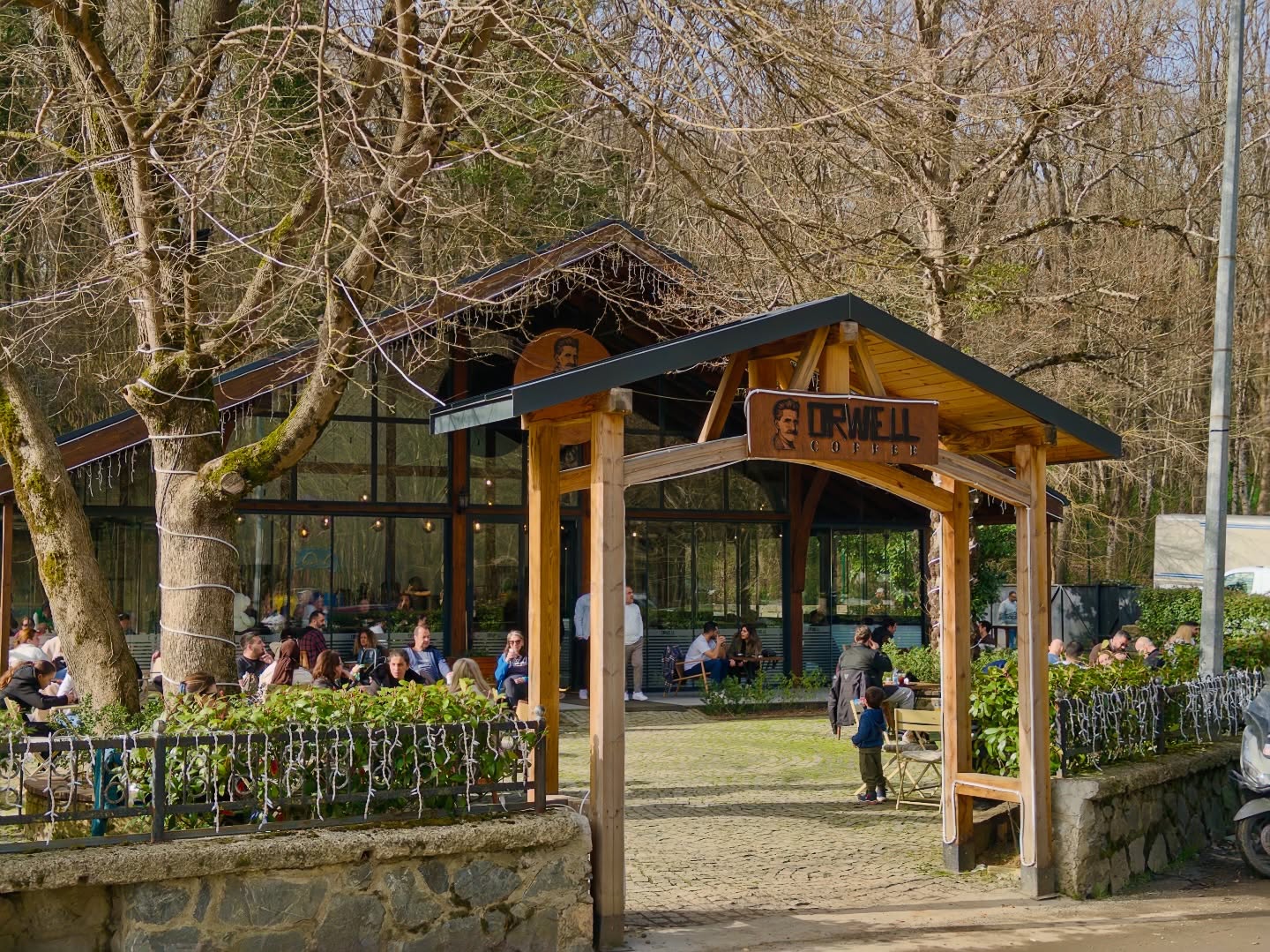 Orwell Coffee Ayvad Bendi şubesinin orman içindeki ahşap giriş kapısı, cam cephesi ve açık oturma alanı